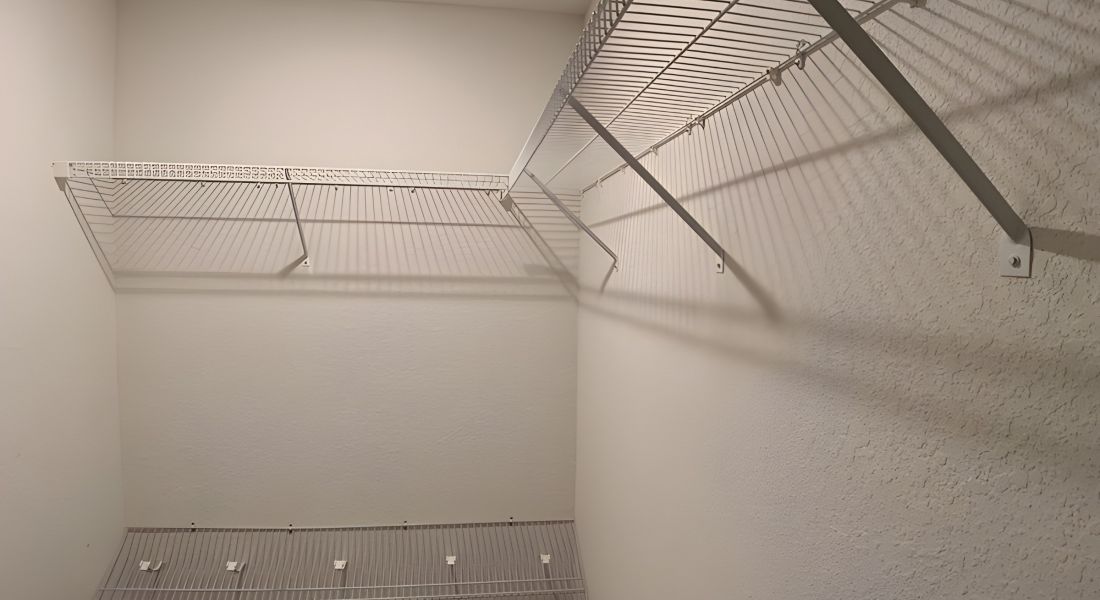 Empty walk-in closet with white wire shelves on the walls and a brown floor.