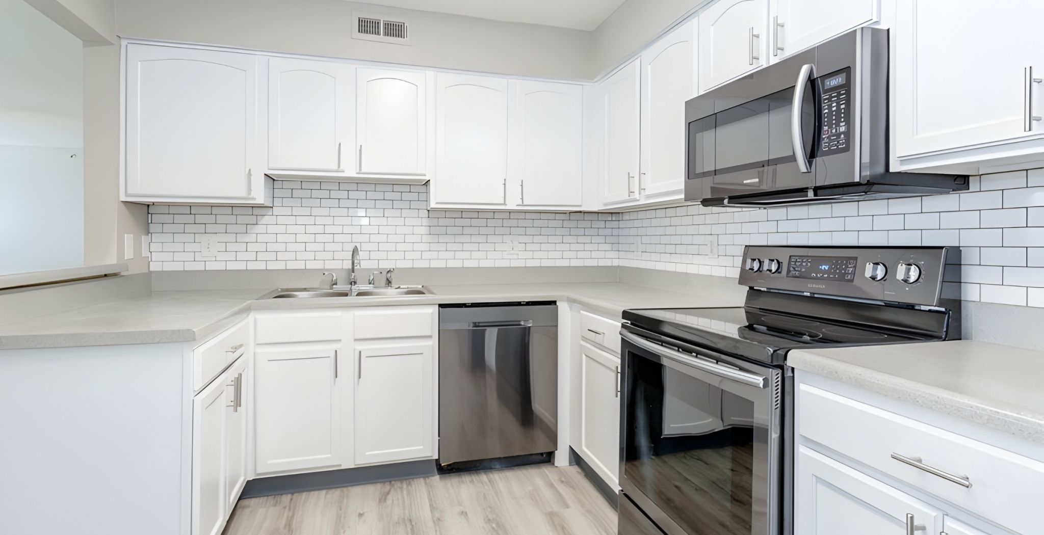 Modern kitchen with stainless steel appliances, white cabinets, and a view into a laundry room with washer and dryer.