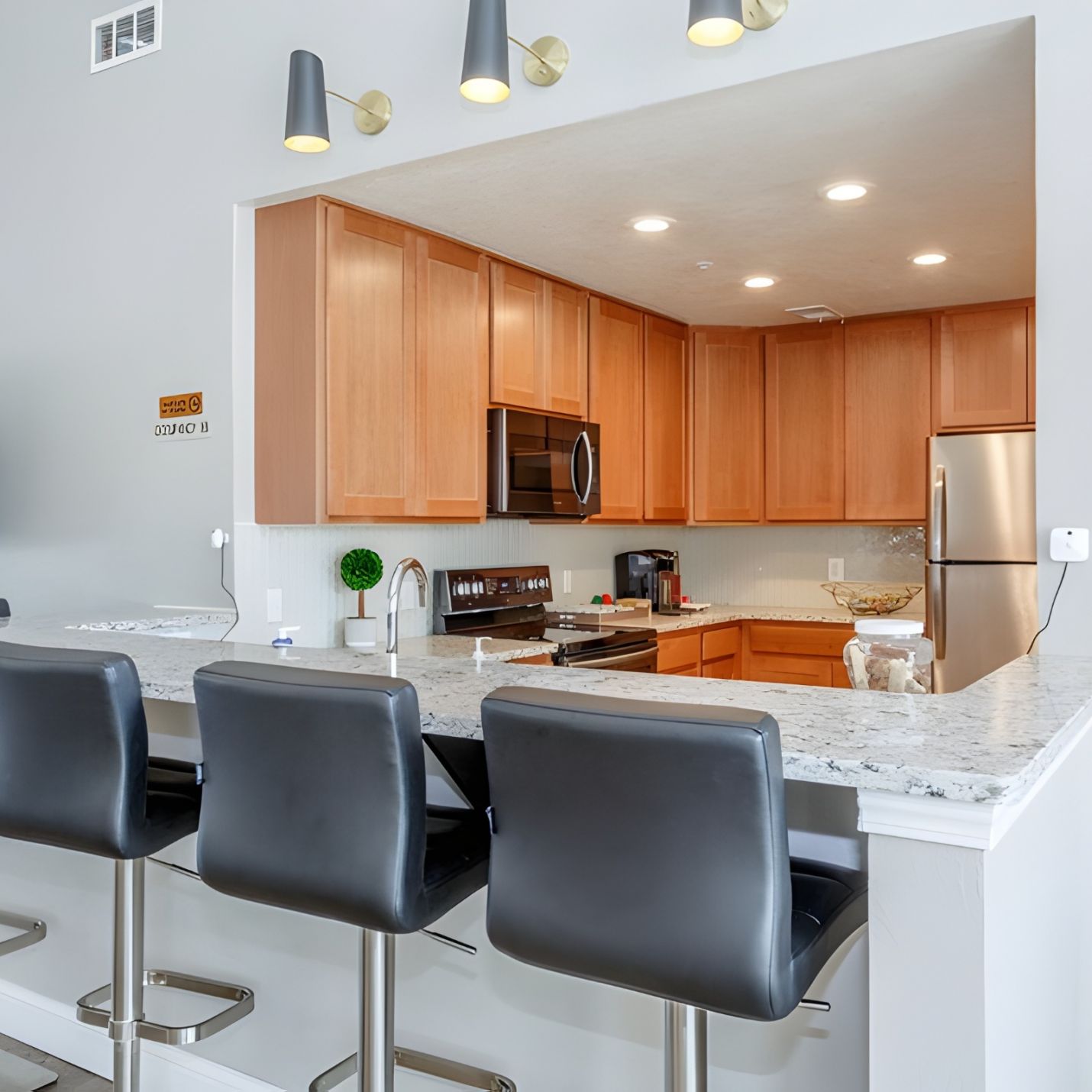 Modern kitchen with wood cabinets, marble countertop, and four black bar stools at a breakfast bar.