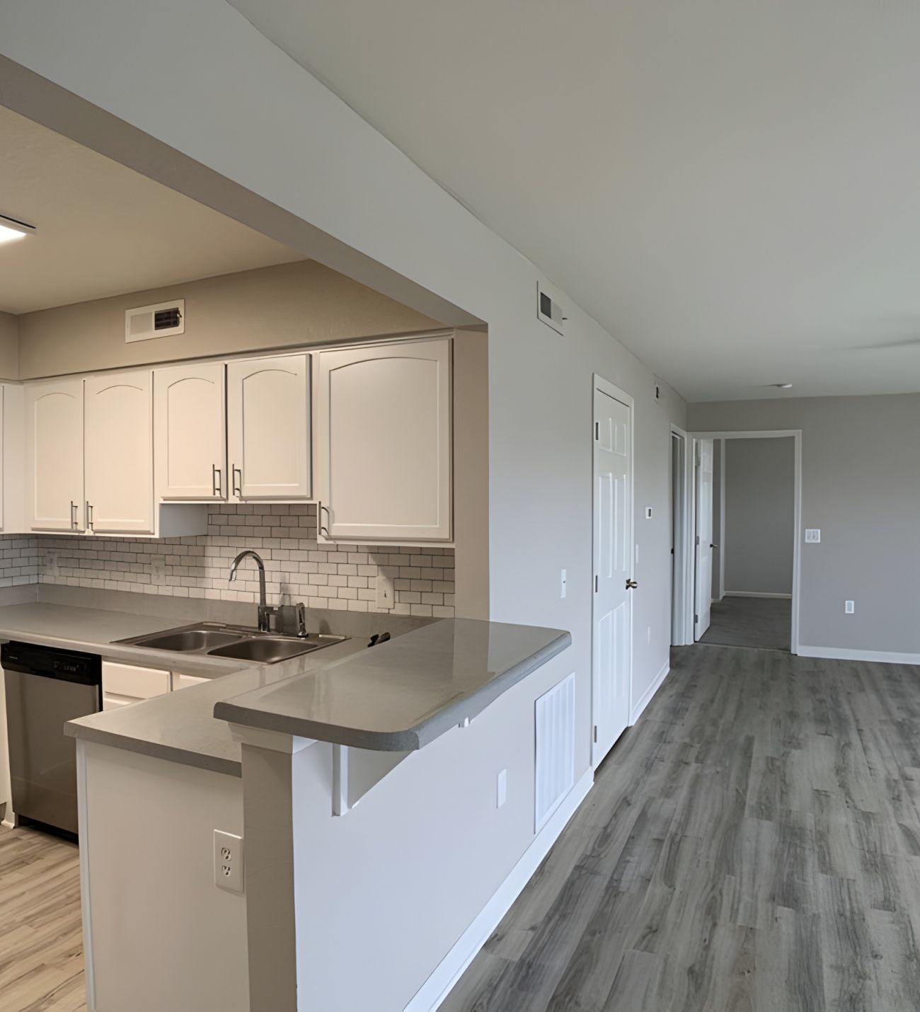 Modern apartment kitchen with white cabinets and open living area featuring wood-style flooring.