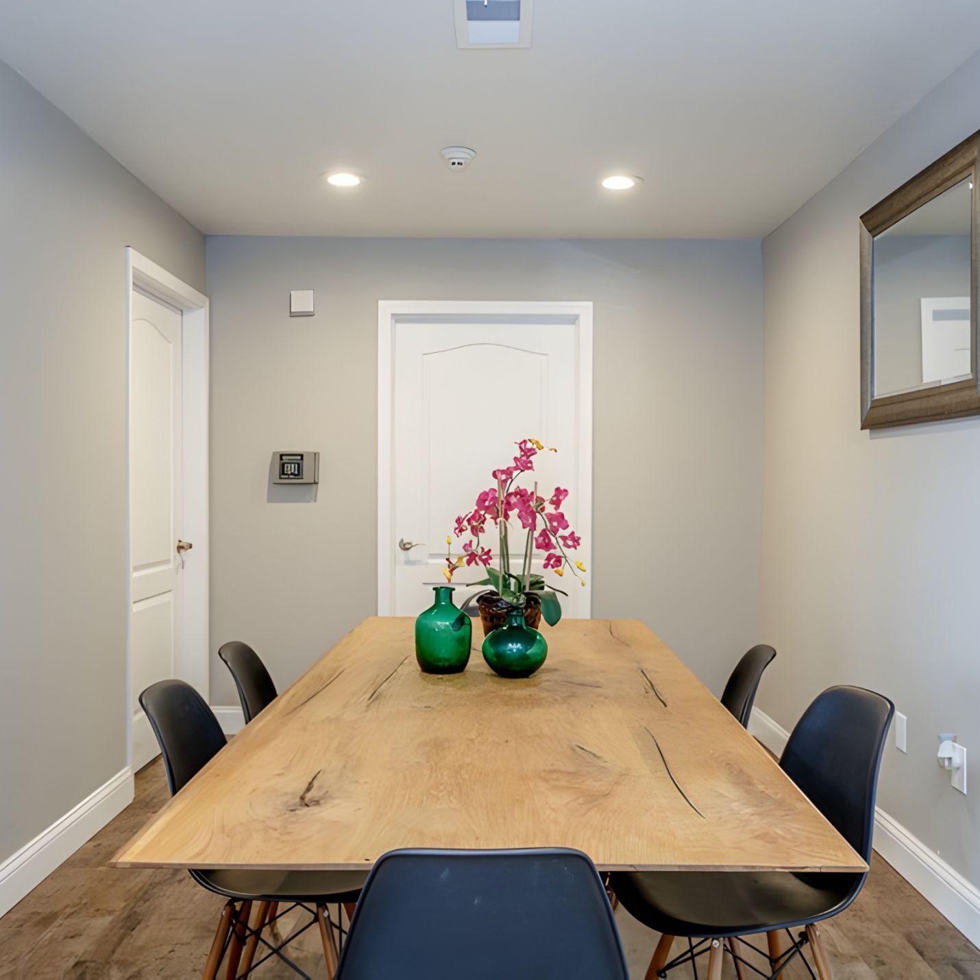 Modern dining room with a wooden table, black chairs, and pink flowers in green vases as centerpiece.