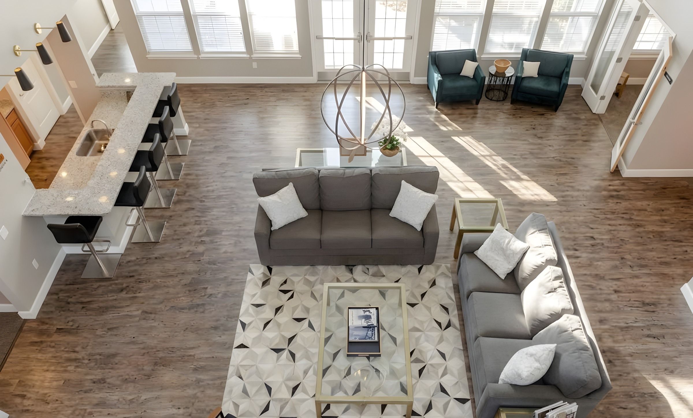 Modern living room with gray sofas, armchairs, a geometric rug, and a kitchen island with barstools.